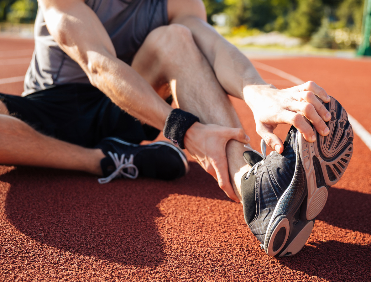 Corredor sentado en pista de atletismo tocando la zapatilla deportiva